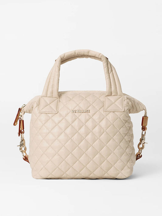 The MZ Wallace Small Sutton Deluxe in Buff Oxford is a beige quilted handbag with short handles and gold hardware, featuring a detachable brown crossbody strap, zipper closure, and elegant Italian leather trim for added luxury.