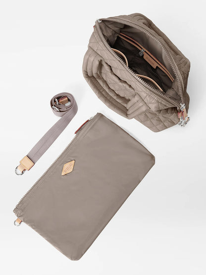 The MZ Wallace Small Sutton Deluxe in Morning Dove Oxford is shown with its interior visible through an open zipper, alongside a matching detachable strap and a flat zippered pouch, all displayed on a white background.
