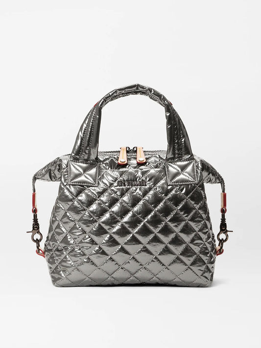 The MZ Wallace Small Sutton Deluxe in Pewter Metallic Oxford is a handbag made from natural Italian leather with a quilted design. It features two handles, a detachable shoulder strap, exterior pockets, and a gold zipper closure on a neutral background.