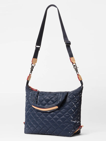 The MZ Wallace Small Sutton Deluxe in Ink Liquid Oxford is a navy quilted crossbody bag with adjustable strap, top handles, and Italian leather trim, shown against a plain white background.