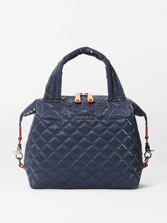 The MZ Wallace Small Sutton Deluxe in Ink Liquid Oxford is a navy blue, quilted handbag with Italian leather trim, short handles, and silver hardware, shown against a plain white background.