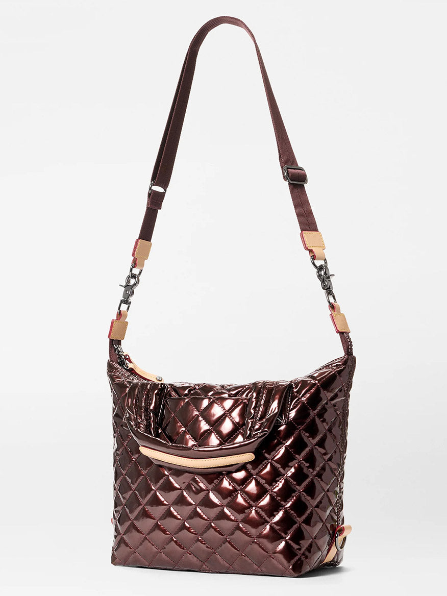 The MZ Wallace Small Sutton Deluxe in Bordeaux Lacquer Oxford is a quilted, shiny dark brown crossbody bag with an adjustable strap, beige accents, Italian leather trim, and a front pocket, shown on a white background.