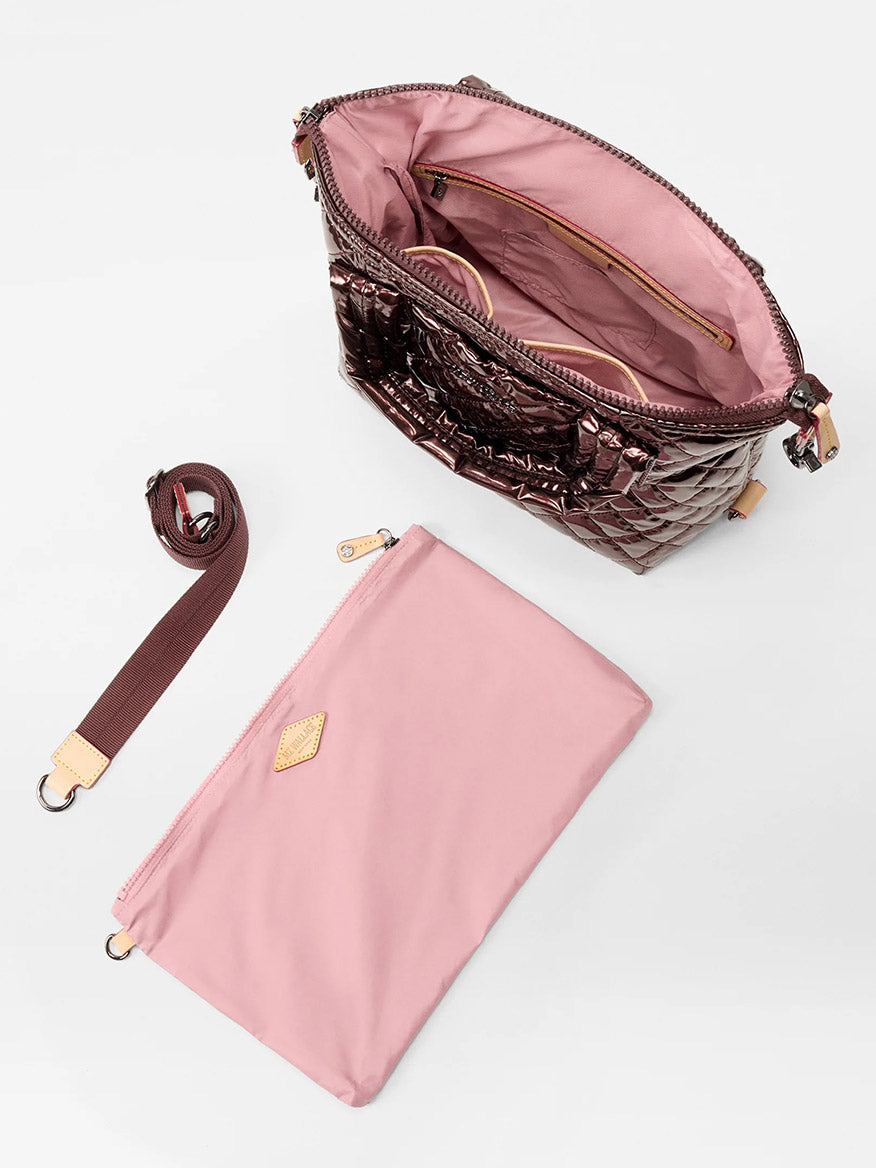 The MZ Wallace Small Sutton Deluxe in Bordeaux Lacquer Oxford is displayed open, revealing a pink interior, Italian leather trim, a detachable shoulder strap, and a separate pink pouch on a white surface.