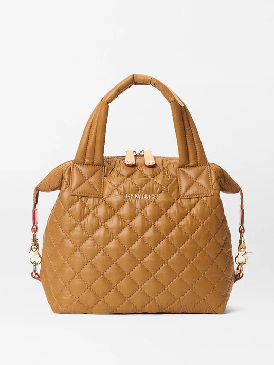 The MZ Wallace Small Sutton Deluxe in Amber Oxford is a tan quilted crossbody bag with short handles, gold-tone hardware, zip closure, and an embossed front logo.