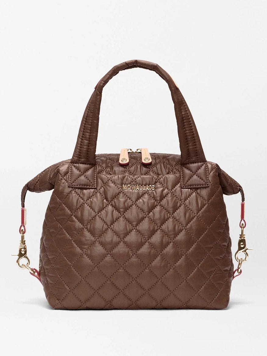 The MZ Wallace Small Sutton Deluxe in Walnut Oxford is a quilted brown handbag crafted from recycled Oxford nylon, featuring two handles, gold-tone hardware, side clips, and a zippered top. A subtle logo accents the front, and the bag can also be worn as a crossbody for versatile styling.
