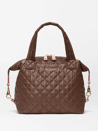 The MZ Wallace Small Sutton Deluxe in Walnut Oxford is a quilted brown handbag crafted from recycled Oxford nylon, featuring two handles, gold-tone hardware, side clips, and a zippered top. A subtle logo accents the front, and the bag can also be worn as a crossbody for versatile styling.