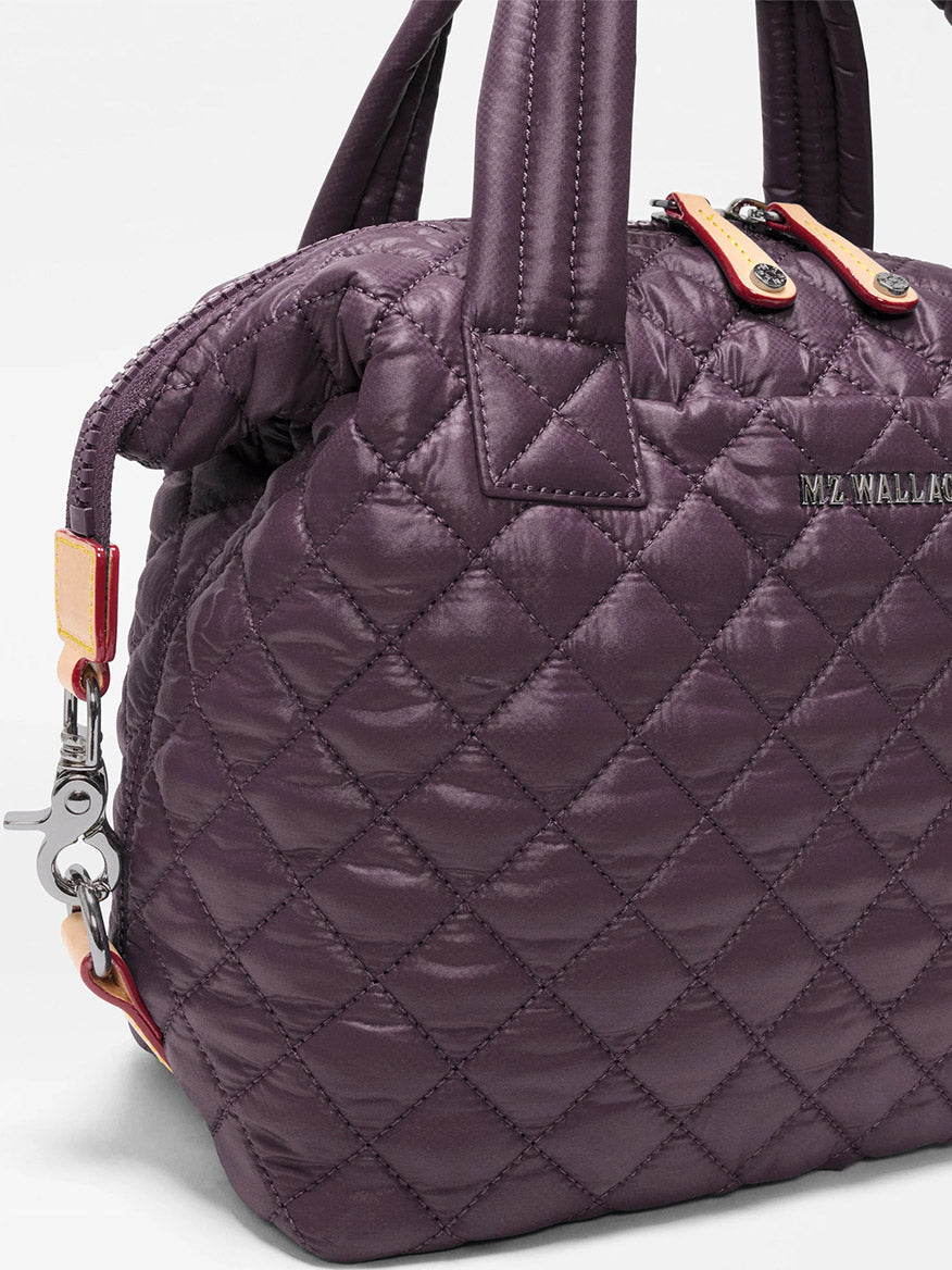 The MZ Wallace Small Sutton Deluxe in Raisin Oxford is a quilted purple handbag made from recycled Oxford nylon, featuring short handles, a zipper closure, and “MZ WALLACE” branding on the side—a compact crossbody bag perfect for carrying your everyday essentials.