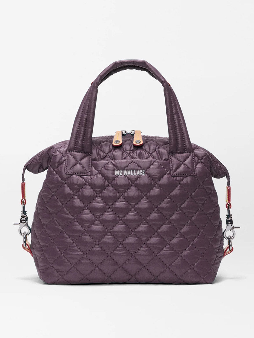 The MZ Wallace Small Sutton Deluxe in Raisin Oxford is a quilted dark purple handbag made from recycled Oxford nylon, featuring two short handles, a zip closure, and detachable shoulder strap hooks on each side, displayed against a plain white background.