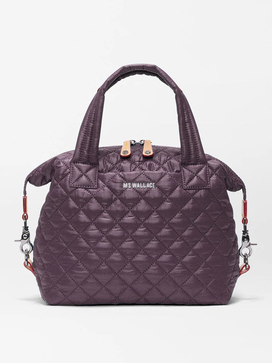 The MZ Wallace Small Sutton Deluxe in Raisin Oxford is a quilted dark purple handbag made from recycled Oxford nylon, featuring two short handles, a zip closure, and detachable shoulder strap hooks on each side, displayed against a plain white background.