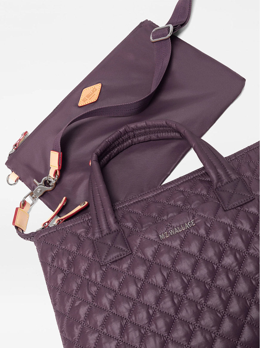Two quilted purple bags with handles and silver hardware, crafted from recycled Oxford nylon, are displayed on a white background. The larger bag features the “MZ WALLACE” logo, while the smaller one—the MZ Wallace Small Sutton Deluxe in Raisin Oxford—serves as a compact crossbody bag with a detachable strap.