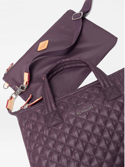 Two quilted purple bags with handles and silver hardware, crafted from recycled Oxford nylon, are displayed on a white background. The larger bag features the “MZ WALLACE” logo, while the smaller one—the MZ Wallace Small Sutton Deluxe in Raisin Oxford—serves as a compact crossbody bag with a detachable strap.