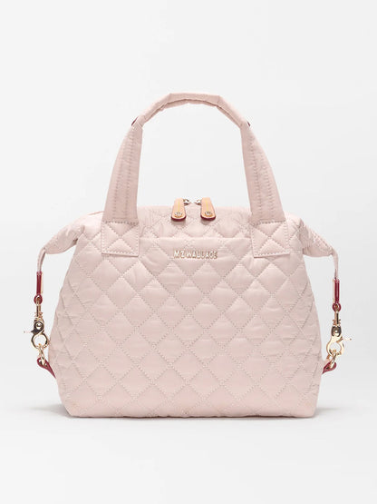 The MZ Wallace Small Sutton Deluxe in City Pink Oxford features quilted nylon, top handles, a zip closure, detachable adjustable crossbody strap, and gold-tone hardware, shown against a plain white background.