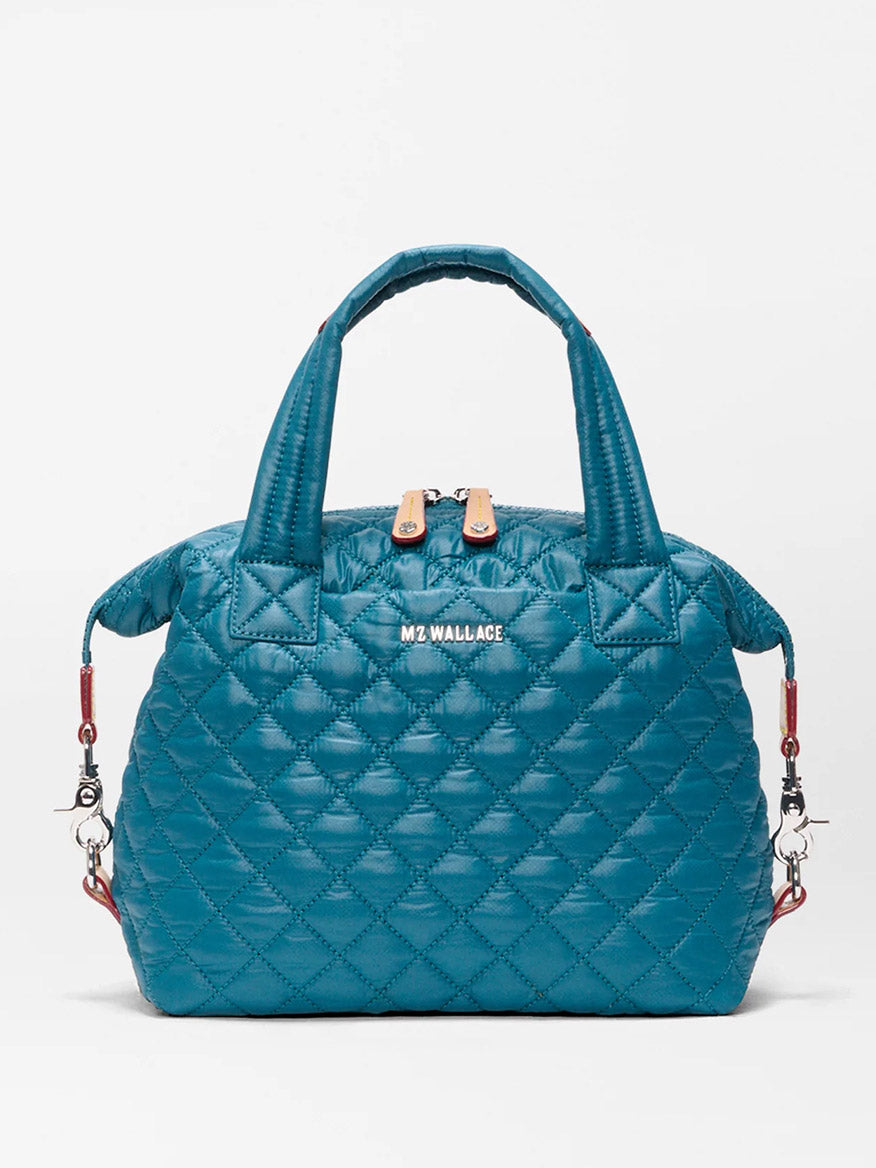 The MZ Wallace Small Sutton Deluxe in Pacific Oxford is a teal quilted nylon bag with short handles, a zip closure, silver hardware, an adjustable crossbody strap, and “MZ WALLACE” on the front.