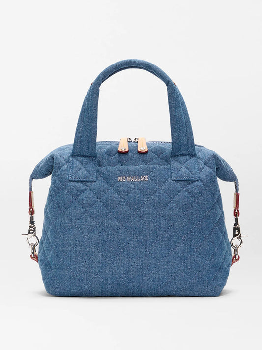 The MZ Wallace Small Sutton Deluxe in True Blue Denim features quilted blue fabric, Italian leather trim, two short handles, a zipper closure, silver "MZ WALLACE" logo, and detachable shoulder strap clips on each side.