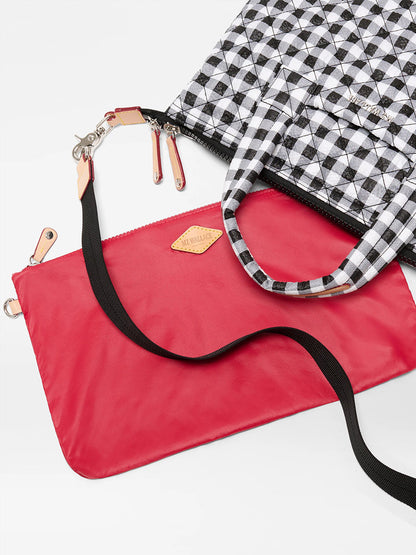 The MZ Wallace Small Sutton Deluxe in Black/White Gingham Oxford sits beside a flat red pouch with an adjustable crossbody strap, both displayed on a white background.