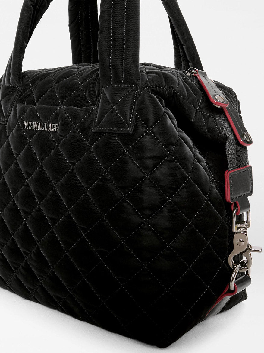 MZ Wallace Small Sutton Deluxe in Black Velvet Finish with a top zipper, dual handles, and a detachable shoulder strap with red accents.