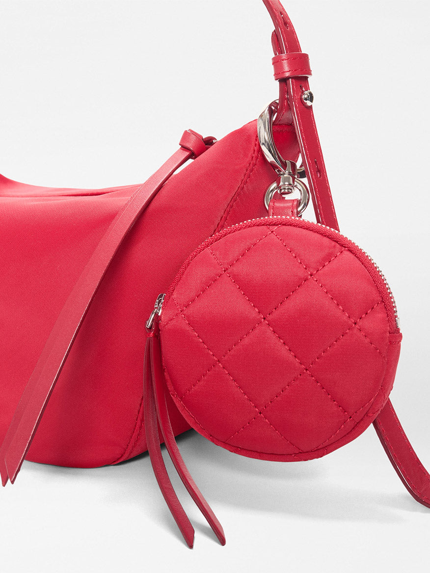 The MZ Wallace Small Waverly Hobo in Apple Bedford is a red handbag with silver hardware, a zip top closure, and a quilted round coin purse attached to its strap.