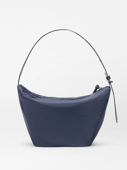 The MZ Wallace Small Waverly Hobo in Dawn Bedford is a navy crescent-shaped handbag with Italian leather, a thin shoulder strap, and zip top closure, displayed on a plain white background.