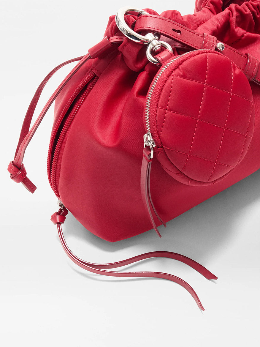 Close-up of the MZ Wallace Small Waverly Shoulder in Apple Bedford, featuring red leather, a drawstring closure, silver hardware, a crossbody strap, and an attached small quilted round coin pouch.