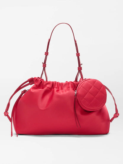 The MZ Wallace Small Waverly Shoulder in Apple Bedford is a bright pink satin bag with thin handles, a crossbody strap, drawstring closure, and a small quilted round pouch on the front.