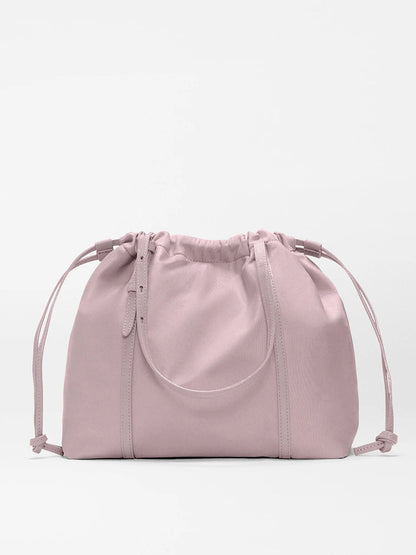 The MZ Wallace Small Waverly Tote in Quail Bedford is a light pink drawstring bag with short handles, made from recycled nylon and detailed with Italian leather trim, shown on a plain white background.