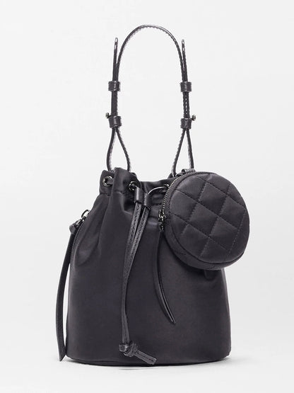 The MZ Wallace Waverly Bucket Bag in Black Bedford features a drawstring closure, shoulder straps, Italian leather trim, and a small round quilted pouch on the front, showcased against a plain light background.