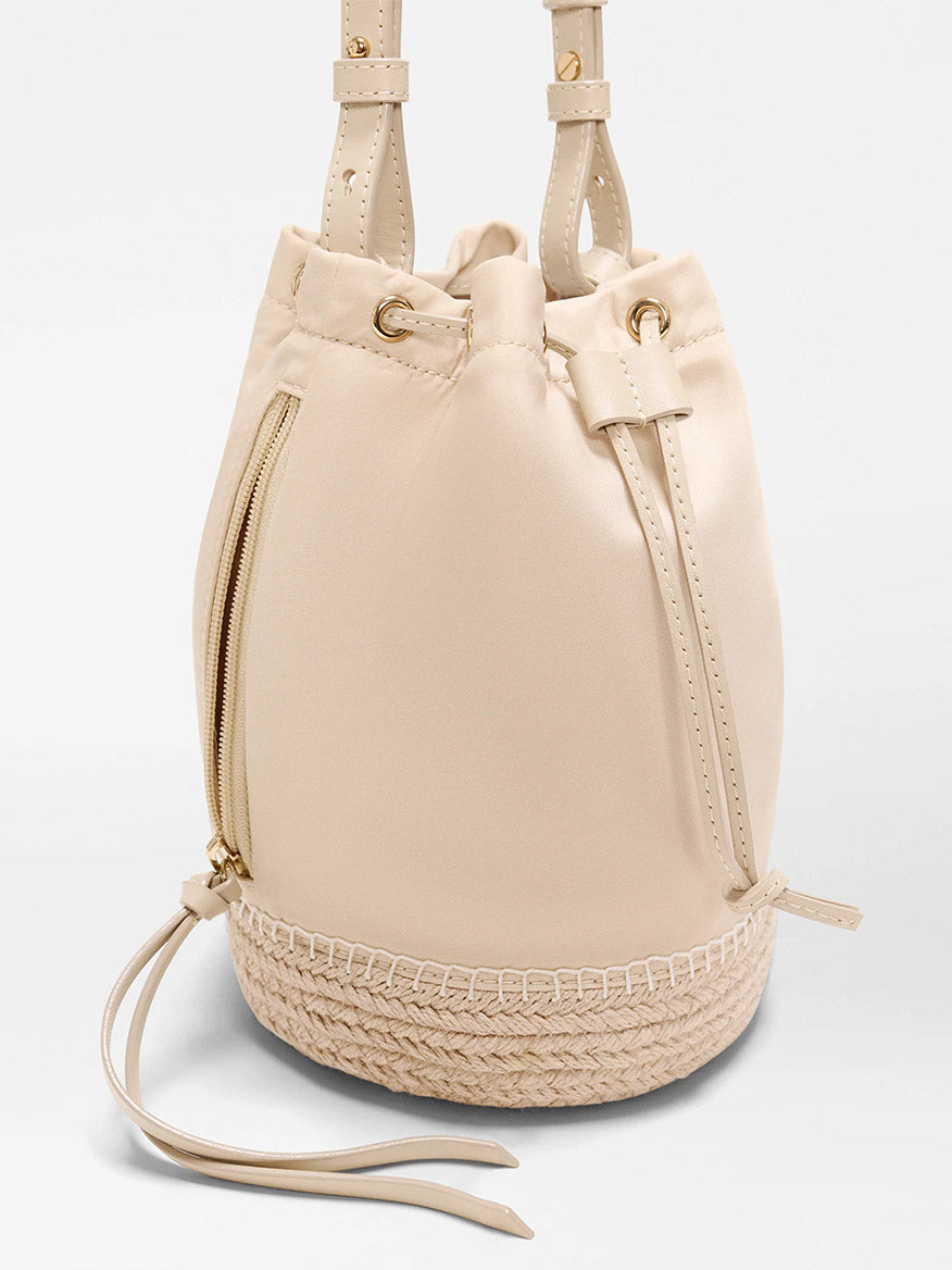 The MZ Wallace Waverly Espadrille Bucket Bag in Buff Bedford features a beige finish, drawstring closure, gold hardware, Italian leather trim, side zipper pocket, beige lining, and a braided woven espadrille base.