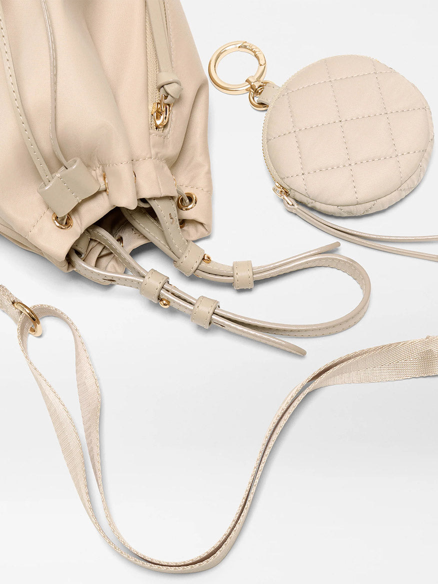 The MZ Wallace Waverly Espadrille Bucket Bag in Buff Bedford features a beige design, gold hardware, Italian leather trim, an adjustable nylon strap, and an attached matching round quilted coin pouch on a keyring.