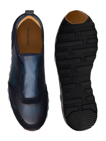 The Magnanni Arco Slip in Navy displayed from both the top and bottom views. The top view showcases its sleek design, while the bottom view highlights the black rubber sole with grooved patterns, complemented by a retro-inspired sport sneaker style enhanced with a stretch-napa gore system.