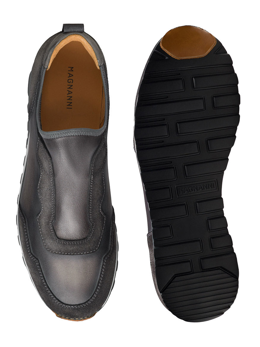 Top and bottom views of the Magnanni Arco Slip in Grey, a single retro-inspired slip-on sport sneaker with black rubber soles, featuring the brand name "Magnanni" on the insole. This design includes a stretch-napa gore system for added comfort.