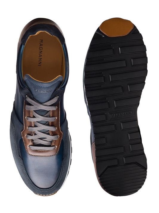 The Magnanni Arco in Navy/Brown is a retro-inspired sneaker featuring a top and sole view with dark laces, blue and brown leather, and a lightweight, flexible black ribbed classic runner sole.