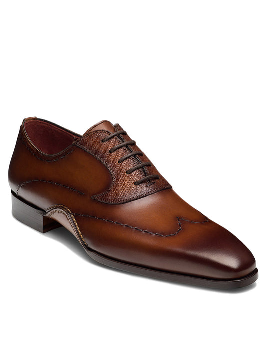 The Magnanni Bowden in Cognac is a brown Wingtip Oxford made from Grabado leather, featuring intricate stitching, perforated details, and dark brown laces, embodying a quintessential Magnanni design for a polished look.