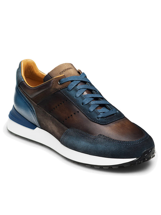 The Magnanni Bravo in Indigo/Brown features a sleek leather sneaker with blue laces, a white midsole, and a black rubber outsole. Its interior boasts a tan lining and intricate leather textures, while its modern sport sole offers enhanced comfort and style.