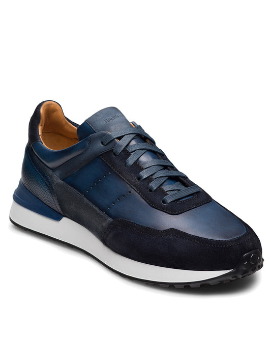 The Magnanni Bravo in Indigo/Navy is a leather Tech Runner sneaker featuring suede accents, a sport sole, blue laces, and tan lining, shown from a front-side angle.