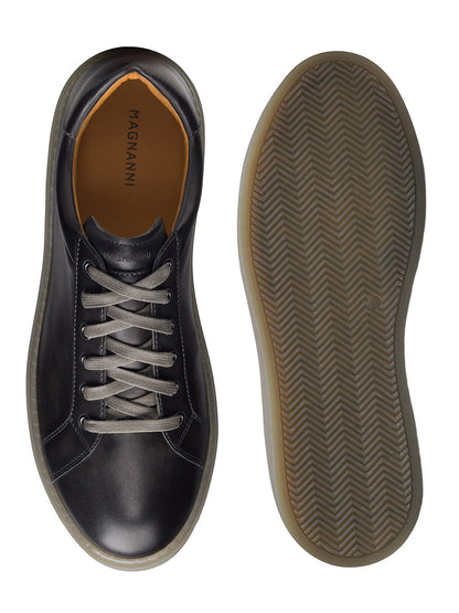 Top and bottom view of a pair of Magnanni Camino Lo sneakers in Grey, featuring black leather cupsoles and gray laces. The brand name "MAGNANNI" is visible on the shoe's insole, and chrome eyelet accents add a touch of sophistication.