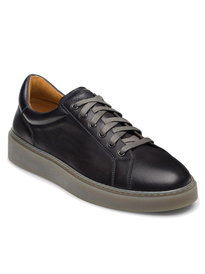 The Magnanni Camino Lo in Grey is a black calfskin leather sneaker with grey laces, chrome eyelet accents, and a tan interior lining. It features a thick grey sole and visible stitching around the edges, embodying the stylish essence of a cupsole fashion sneaker.