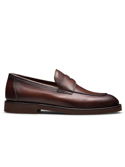 The Magnanni Cervan Penny in Tumbled Brown is a handmade leather slip-on loafer from Portugal, featuring a rounded toe, low heel, and visible stitching, pictured in profile against a white background.
