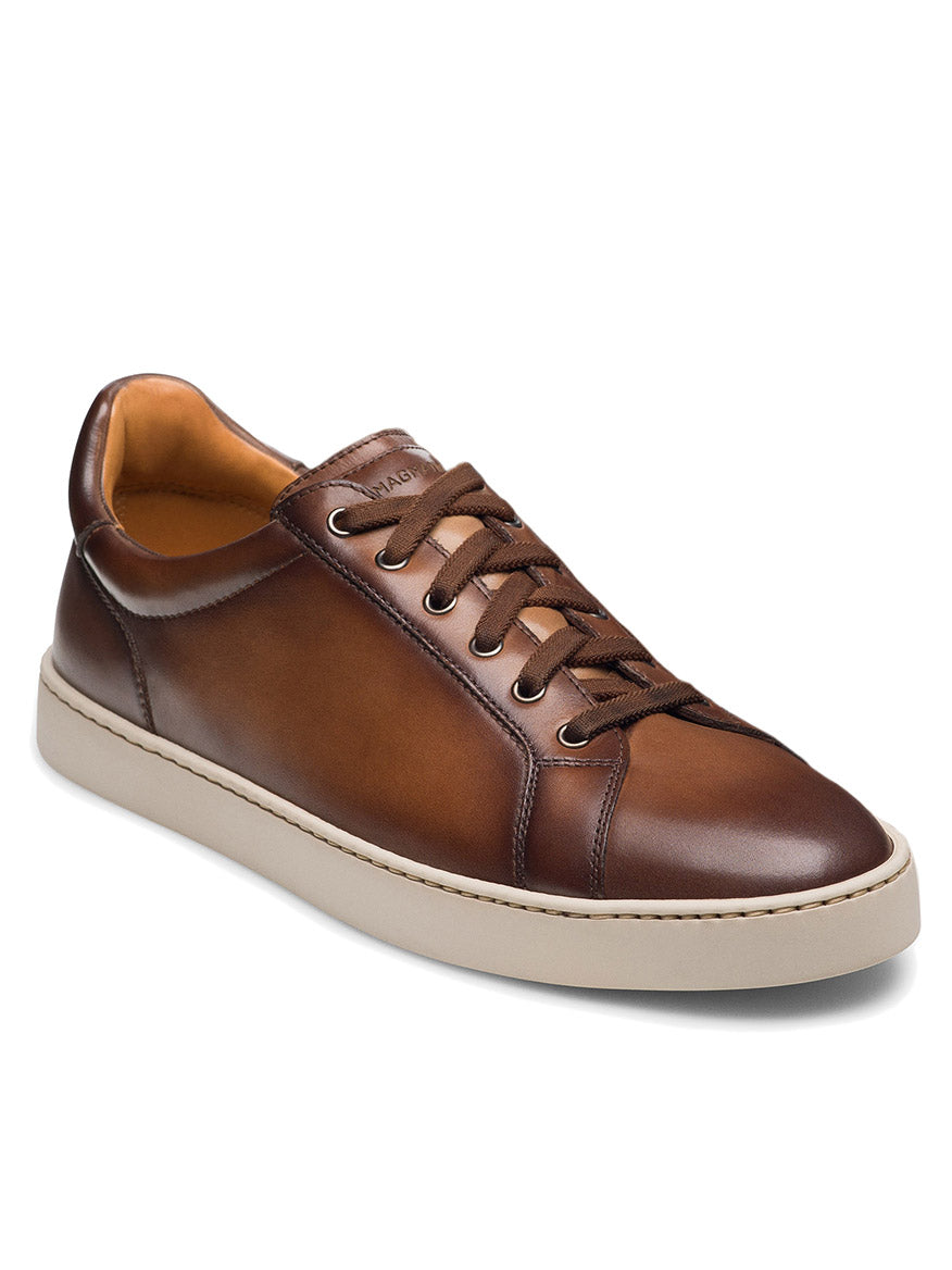 The Magnanni Cote Lo Stretch-Lace in Brown is a men’s low-top sneaker featuring brown leather, stretch laces, a white rubber sole, and stitching detail, shown on a white background.