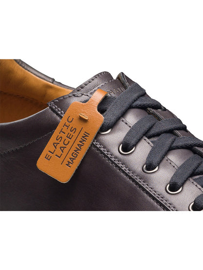 Close-up of the Magnanni Cote Lo Stretch-Lace men’s low-top sneaker in grey leather, featuring a stretch-lace system and a brown tag labeled “ELASTIC LACES MAGNANNI.”.