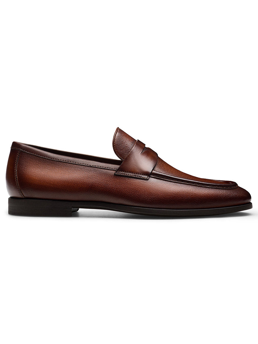 A single Magnanni Dumas penny loafer in Cognac, showcasing a sophisticated textured upper, a low heel, and a sleek, polished finish complemented by a flexible rubber sole.