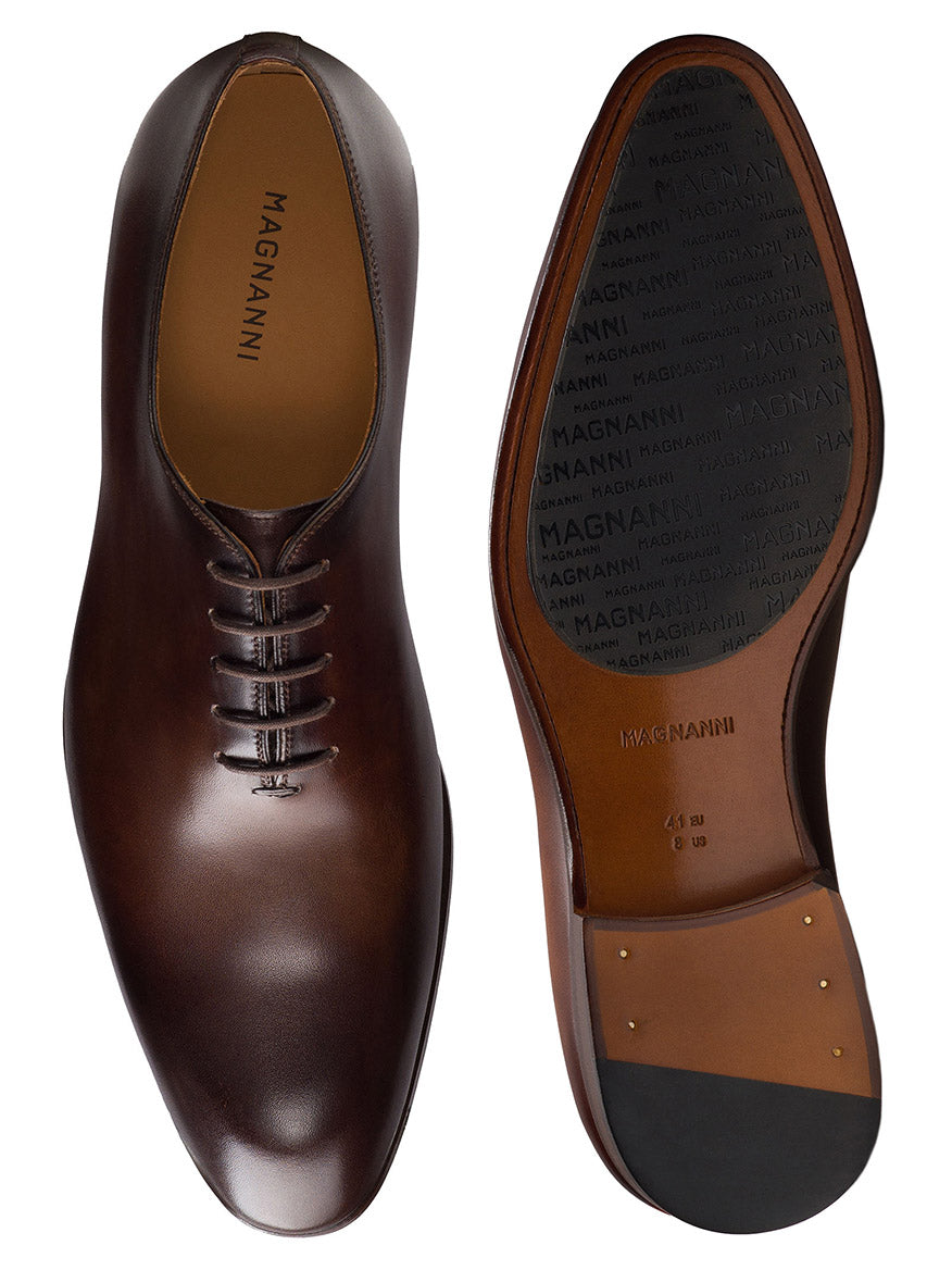 The Magnanni Fleur II in Tabaco men's dress shoes are shown from the top and bottom, featuring a sleek brown leather design, laces, leather sole with rubber grip, and metal toe taps.