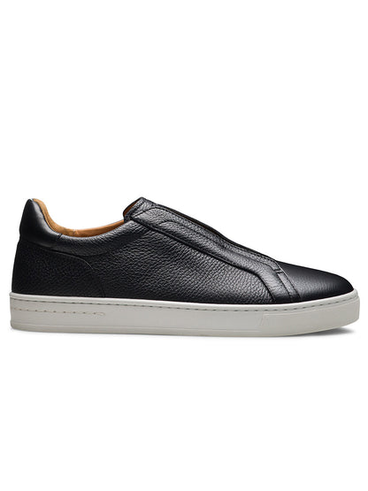 The Magnanni Gasol in Tumbled Black is a black leather slip-on sneaker with a textured surface, hidden elastic gore, and a white rubber sole, displayed from the side against a white background.