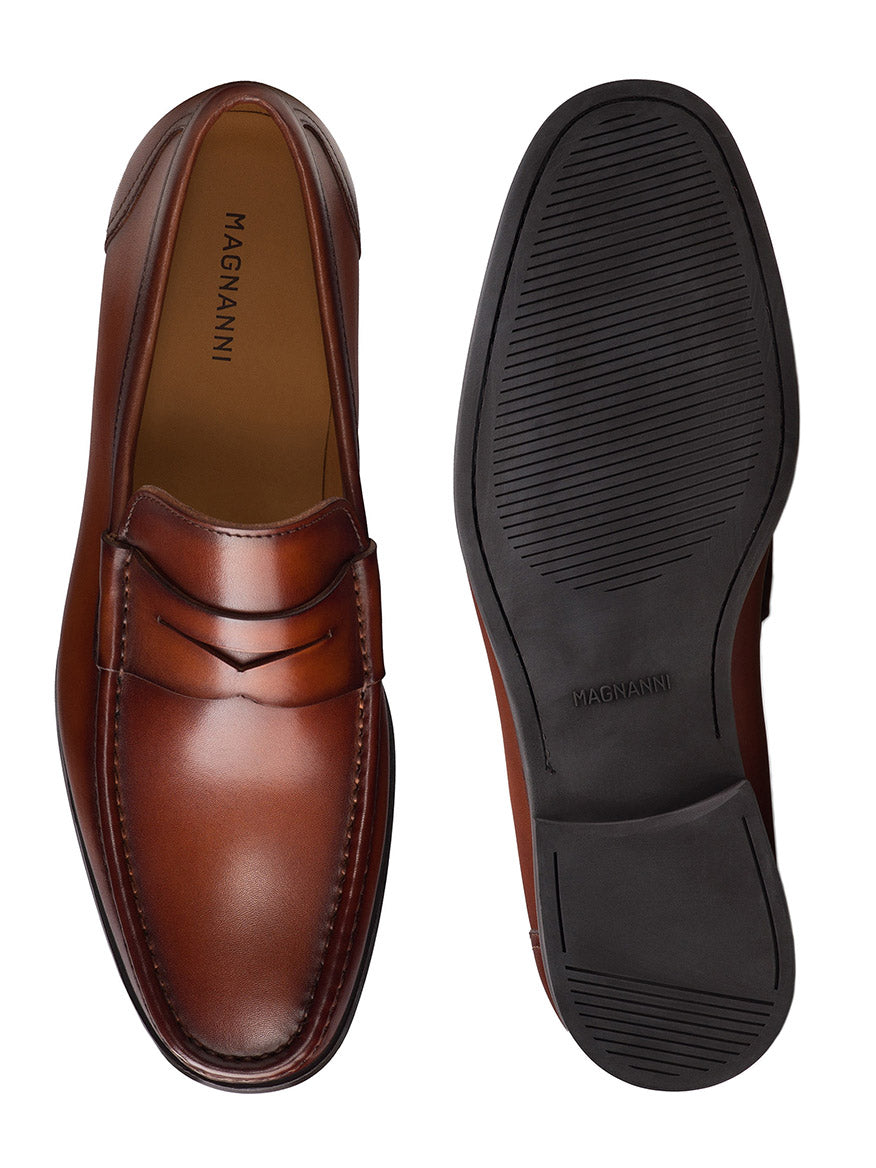 The Magnanni Gentry Penny in Cognac is a pair of brown leather slip-on loafers with a smooth upper and rubber sole, displayed from top and bottom views.