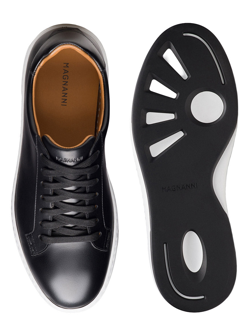 Magnanni Kona Lo in Black low-top sneaker shown from top and bottom views, featuring black laces, tan insole, and a black rubber sole with white trim and a unique cutout pattern on the outsole. This men’s leather sneaker is expertly handmade in Portugal, blending timeless craftsmanship with modern style.