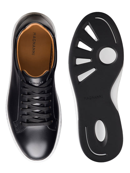 Magnanni Kona Lo in Black low-top sneaker shown from top and bottom views, featuring black laces, tan insole, and a black rubber sole with white trim and a unique cutout pattern on the outsole. This men’s leather sneaker is expertly handmade in Portugal, blending timeless craftsmanship with modern style.