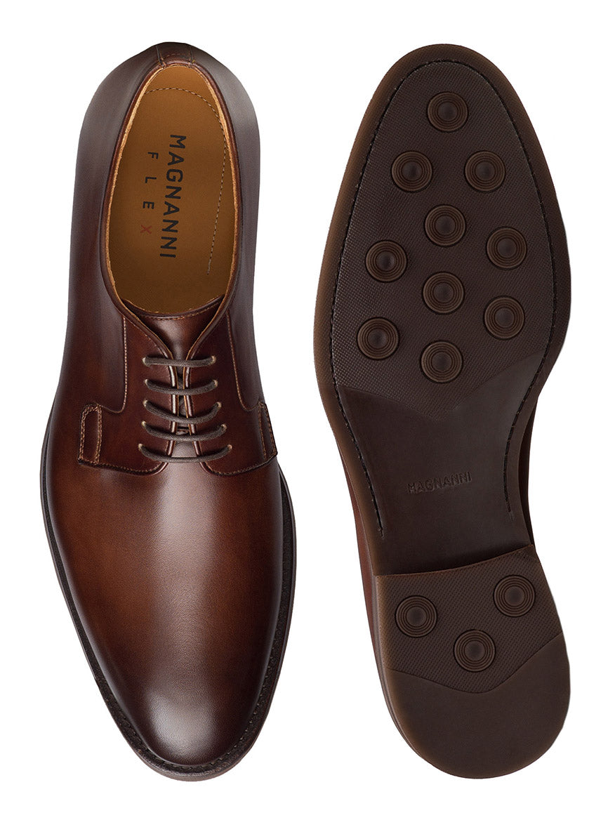 A pair of midbrown Magnanni Lanai dress shoes, shown from the top and bottom. The top view reveals their classic lace-up design, while the bottom view highlights the rubber sole with circular grips. These smart-casual derby shoes feature Bologna construction and a cushioned footbed for ultimate comfort.