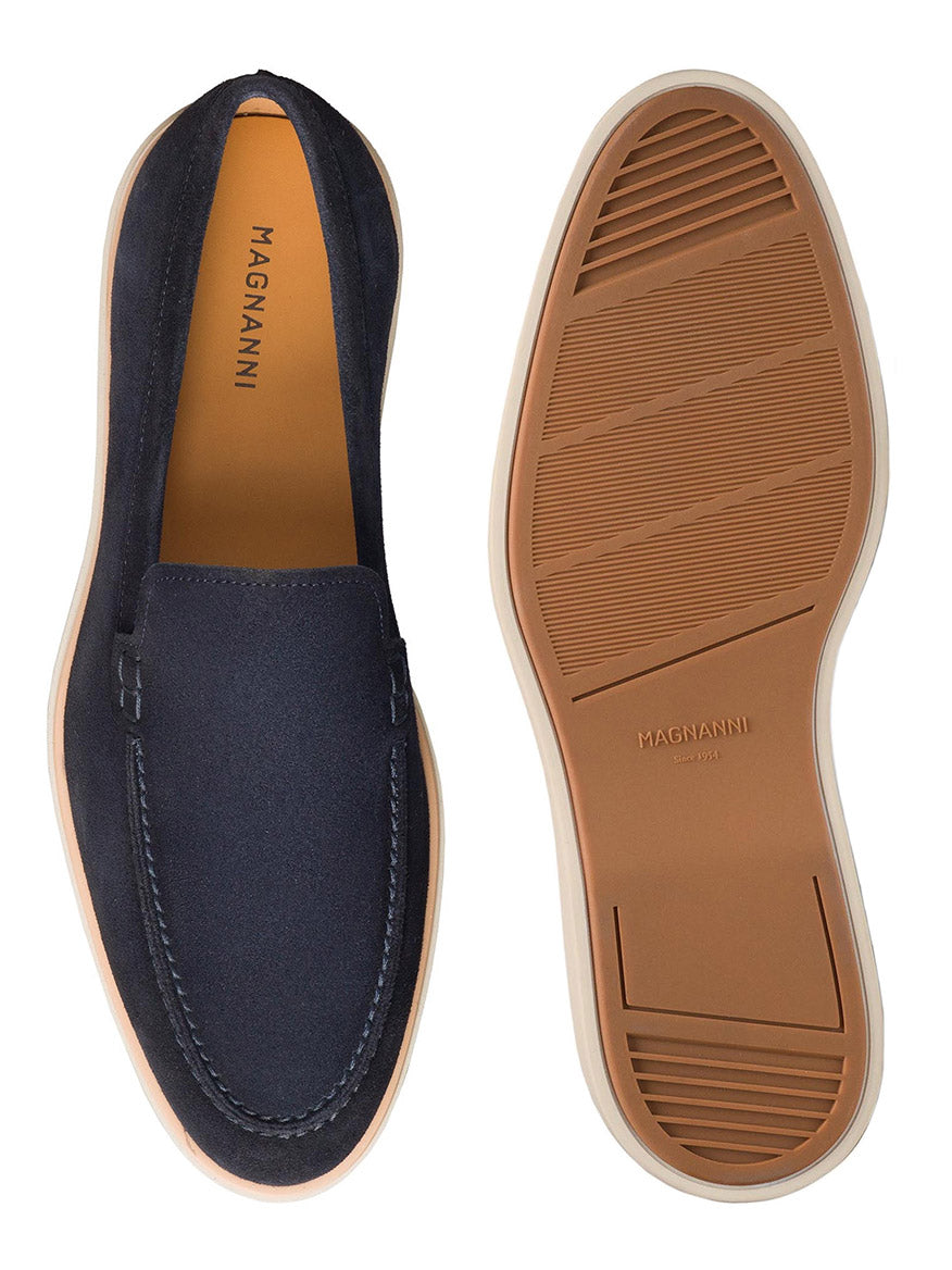 A pair of navy suede apron toe loafers named "Magnanni Lourenco," featuring tan outsoles and "Magnanni" branding on the insole and sole. The shoe on the left is upright, while the one on the right showcases its lightweight rubber sole.