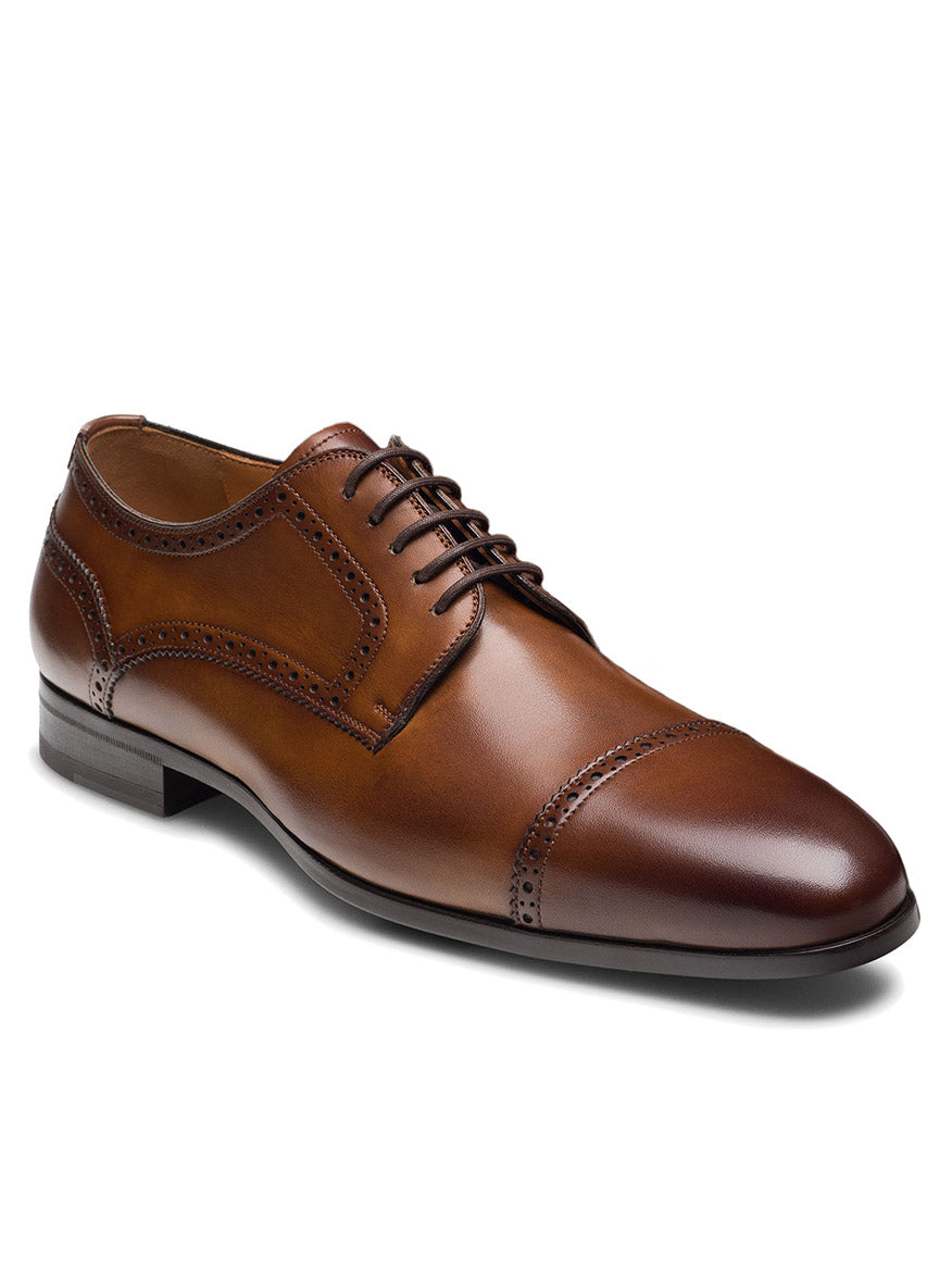 The Magnanni Macsen in Tabaco is a brown leather brogue dress shoe with a cap toe, dark brown sole, and detailed broguing. Featuring handcrafted Bologna construction, this luxury footwear is shown elegantly on a white background.
