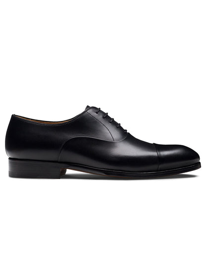 The Magnanni Naxos in Black is a leather Oxford dress shoe with closed lacing and a cap toe, shown in side profile on a white background—ideal men’s formal footwear to complement any tuxedo.