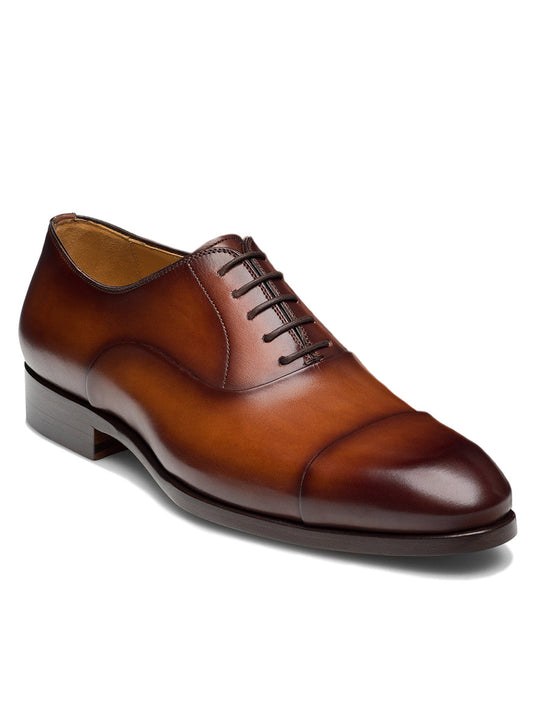The Magnanni Naxos in Cognac is a men's formal brown leather cap toe Oxford with dark brown laces and a low wooden heel, displayed on a white background.